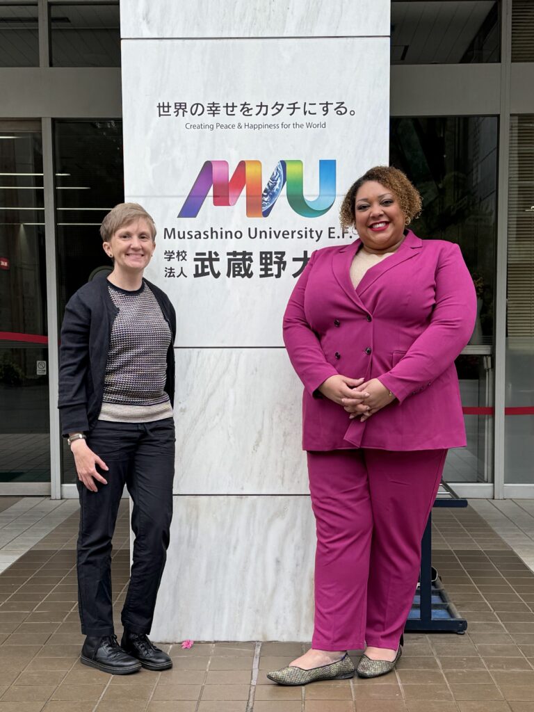 Two people stand in front of a banner sign.
