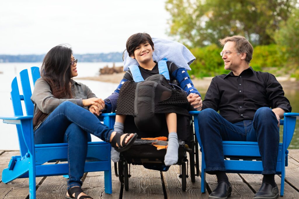 Boy in wheelchair sitting outside with parents.