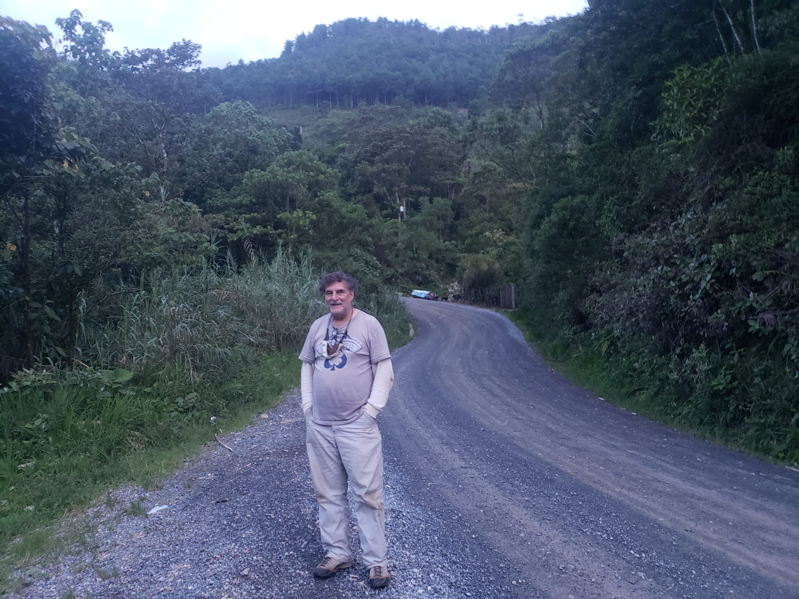 Rich Zack stands to the side of a gravel road. Surrounding him is a dense forest.