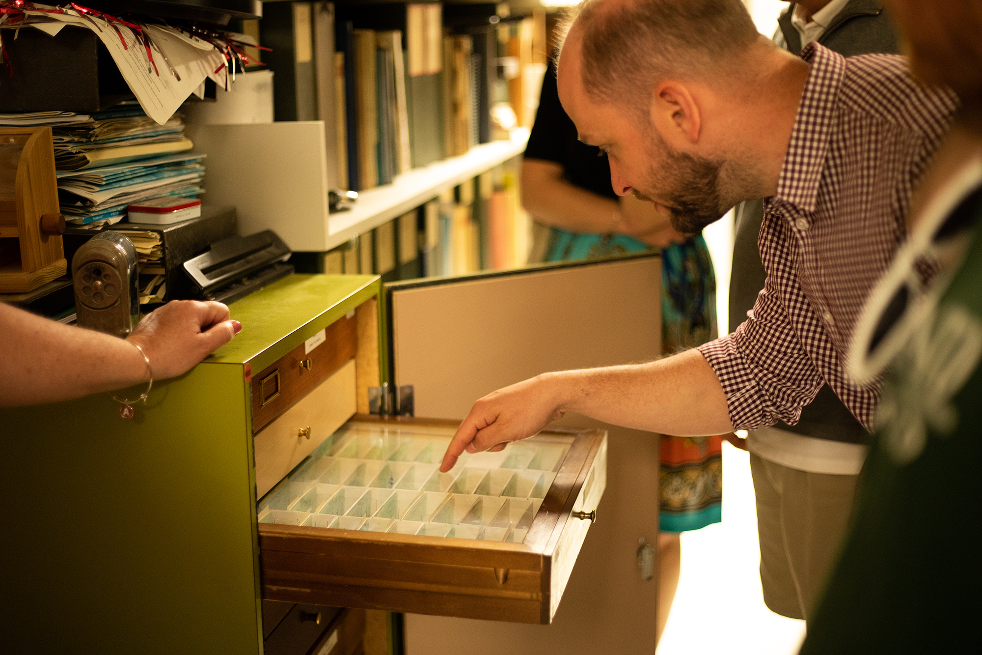 Silas Bossert points at an open drawer in the museum. A few people are gathered around him.