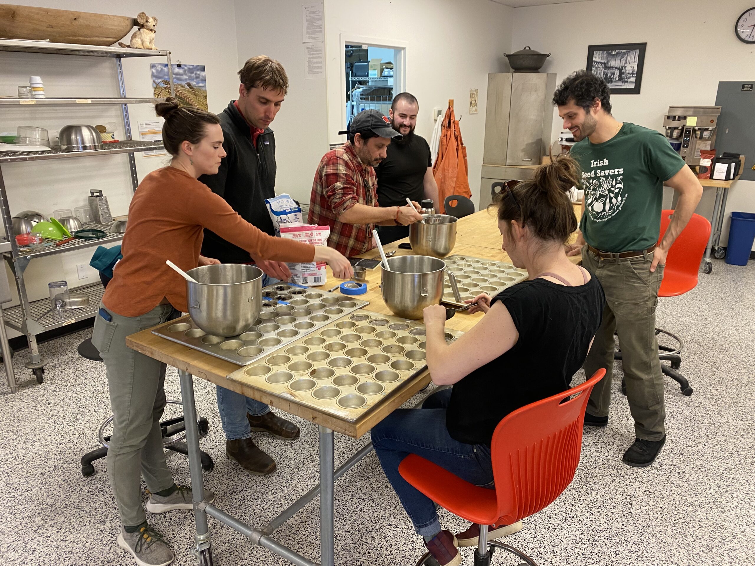 six people gathered around a table filling muffin tins