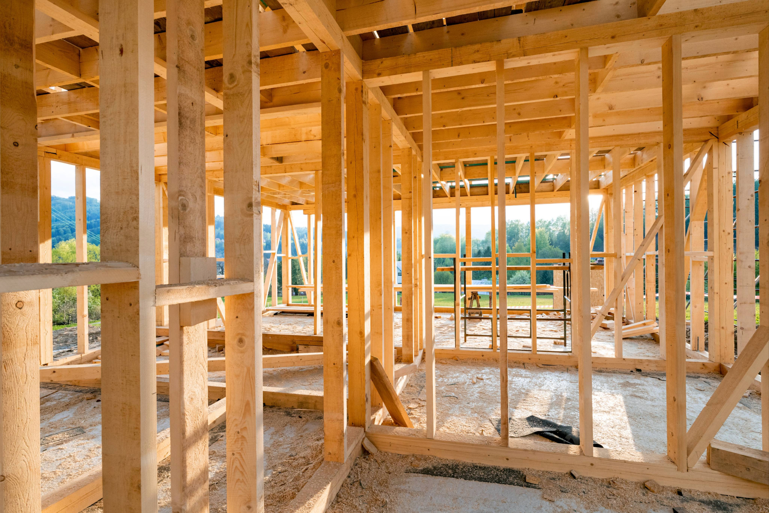 New interior residential wooden construction house framing. Green trees can be seen through the framing. 