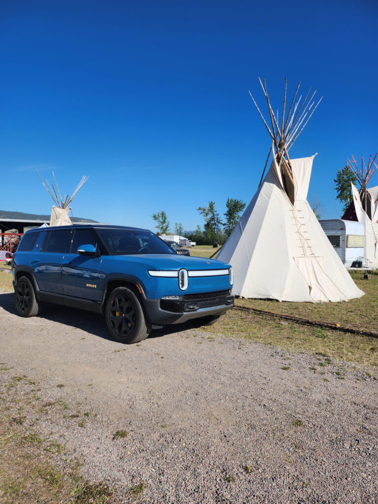 A blue Rivian in front of a teepee.