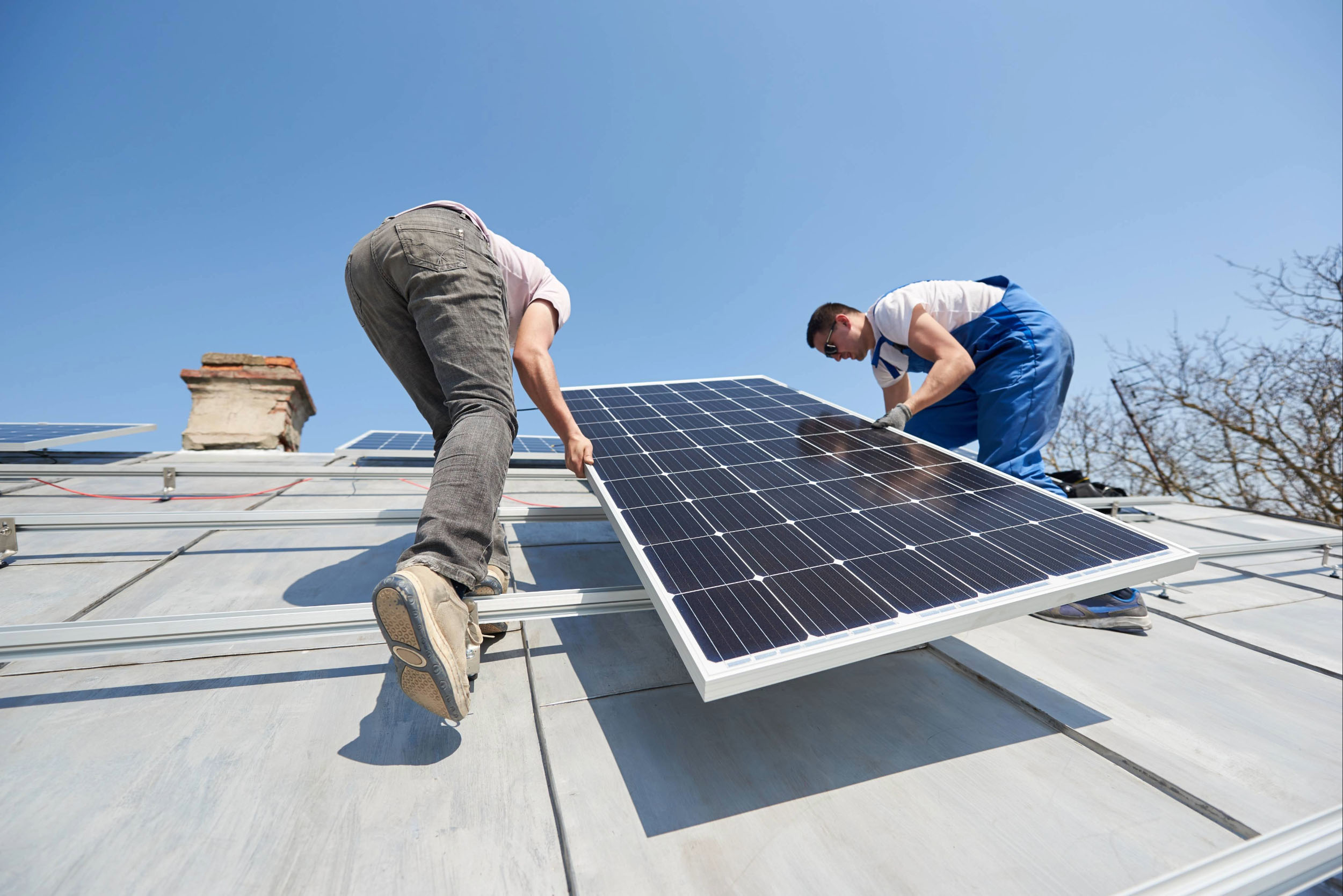 Two workers install solar panels on a roof