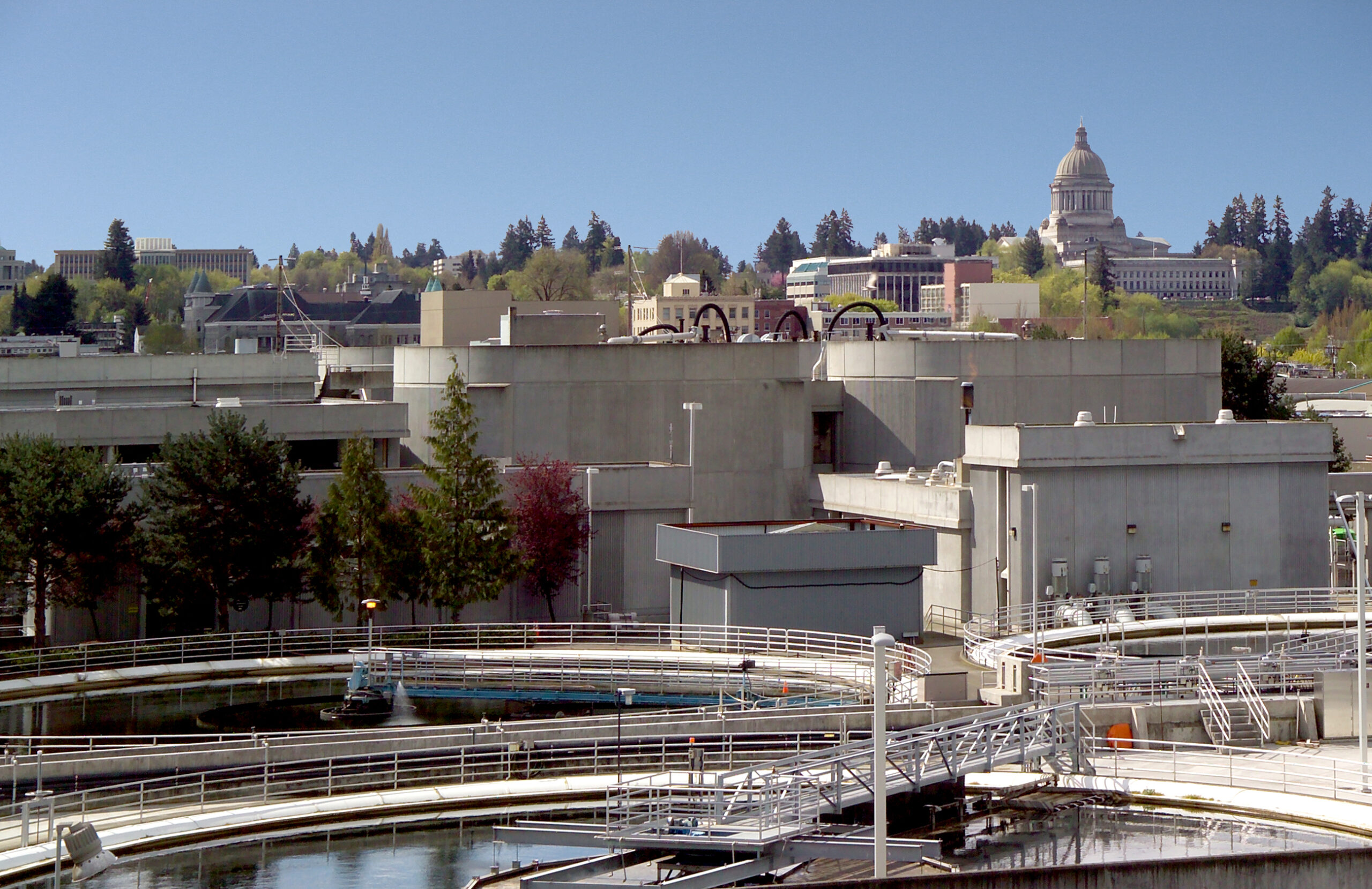 Three anaerobic digester tanks at a water treatment facility. The Washington state capitol peaks out of skyline.