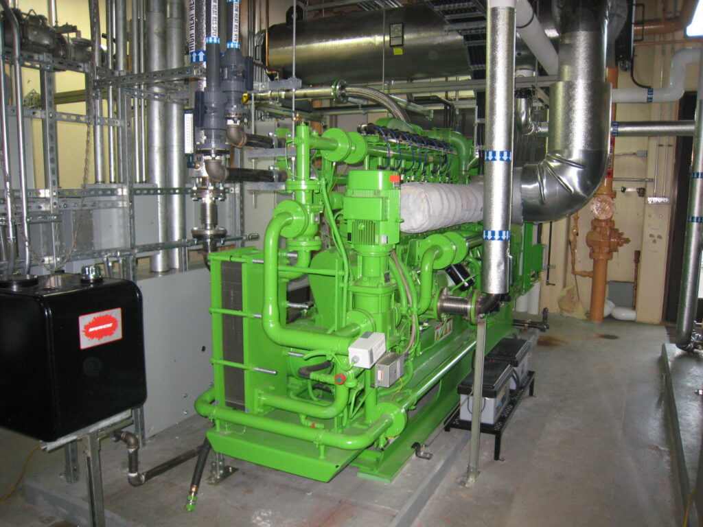 A green reciprocating engine fills a storeroom with many pipes attached.