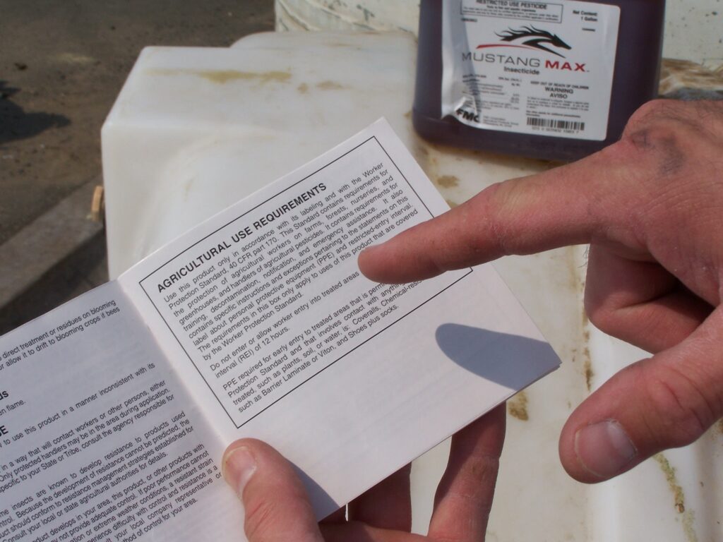 Person pointing at the Agricultural Use Requirements section of a pesticide label.