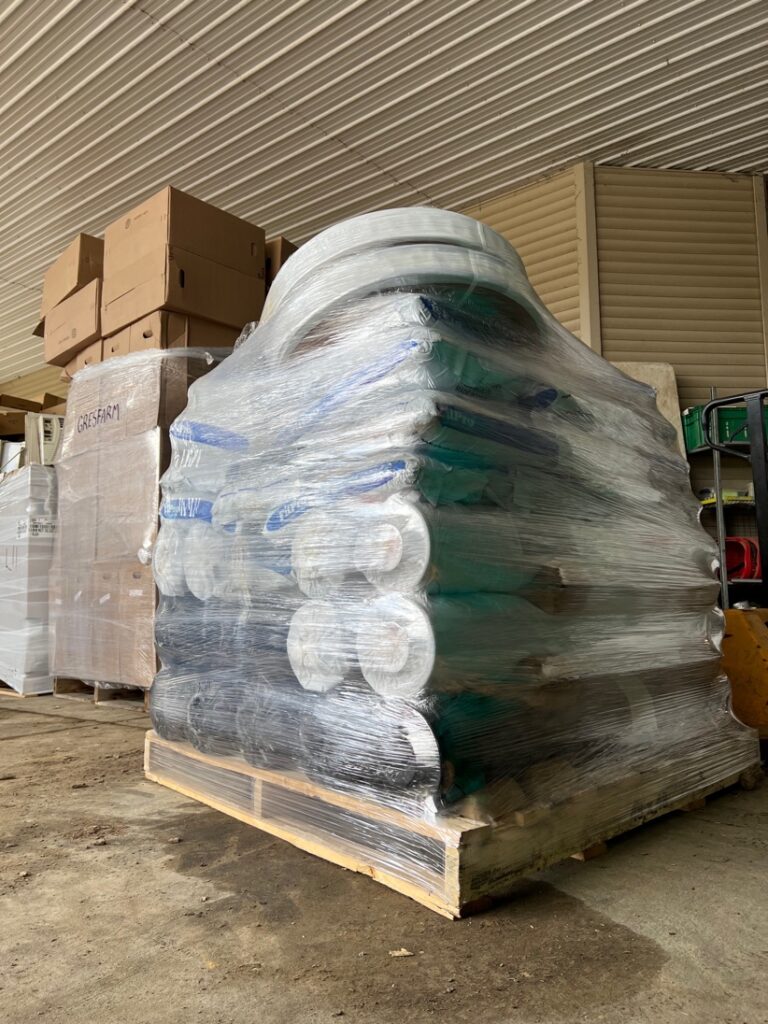 Rolls of plastic mulch stacked horizontally on a pallet and covered in stretch wrap.