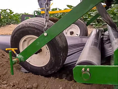 Detail of mulch installation. Sheet passes beneath roller and is guided by pneumatic wheel.