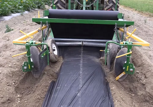 A machine laying down mulch sheet in a field.