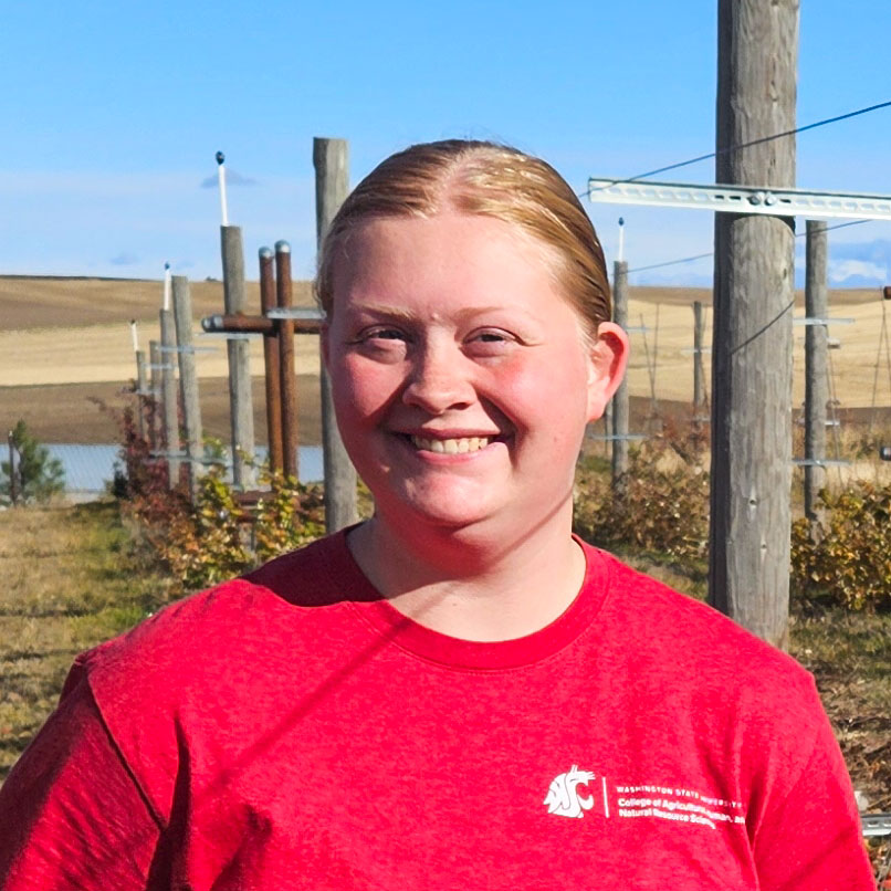 Tessa Berendsen standing in a raspberry field with rolling hills in the distance.