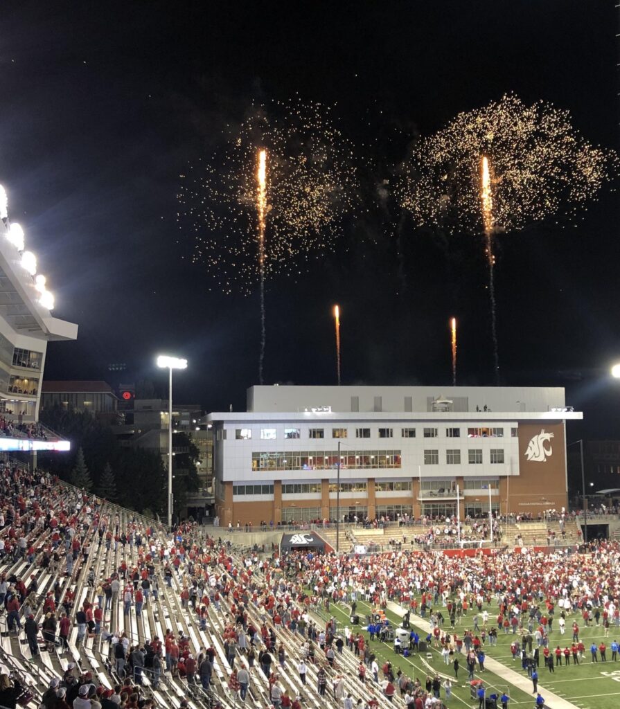 Crowds of people on the field and in the stands of the football stadium at WSU Pullman. Fireworks shoot into the sky.