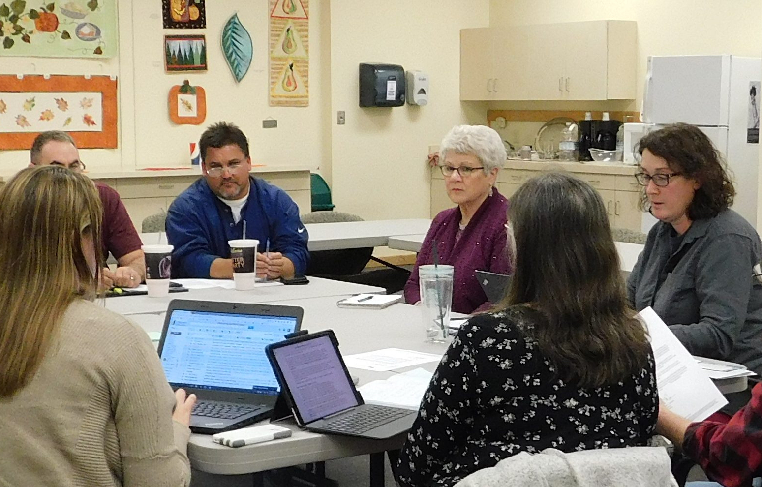 Group of people sitting around a table with their lap tops having a meeting.