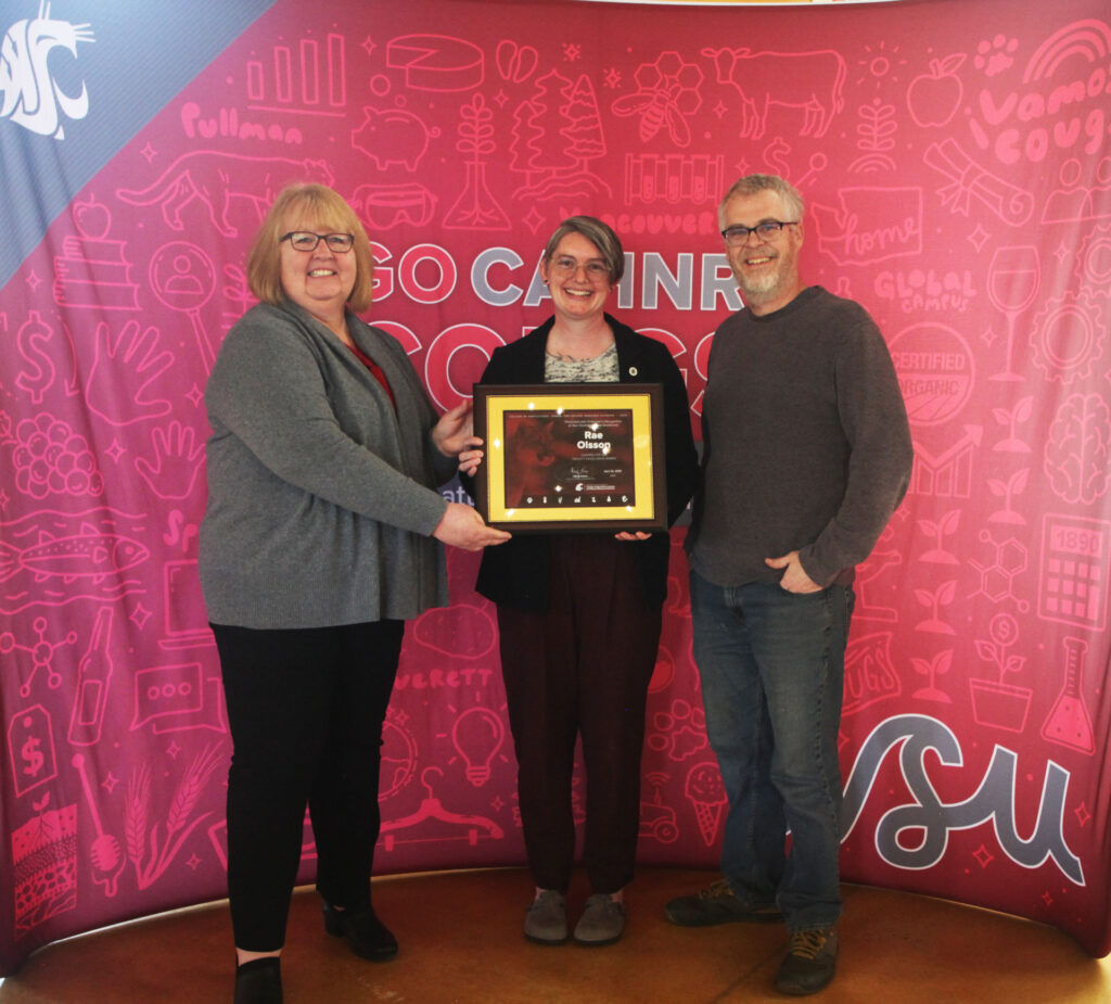 Three people stand together in front of a CAHNRS and WSU-themed background. The person on the left and in the middle hold an award.