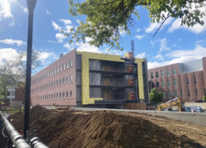 A long 3 story building is shown from the end. The long side looks complete, but the short end side is still mostly open with construction equipment all around.