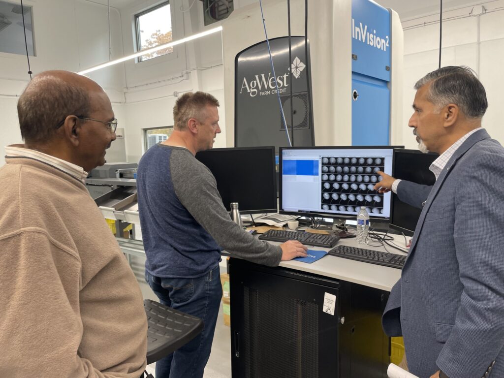 McCord, at console, shows Rayapati and Khosla black and white images of cherries on a screen. A large machine in the background is marked "AgWest Farm Credit" and "InVision2".