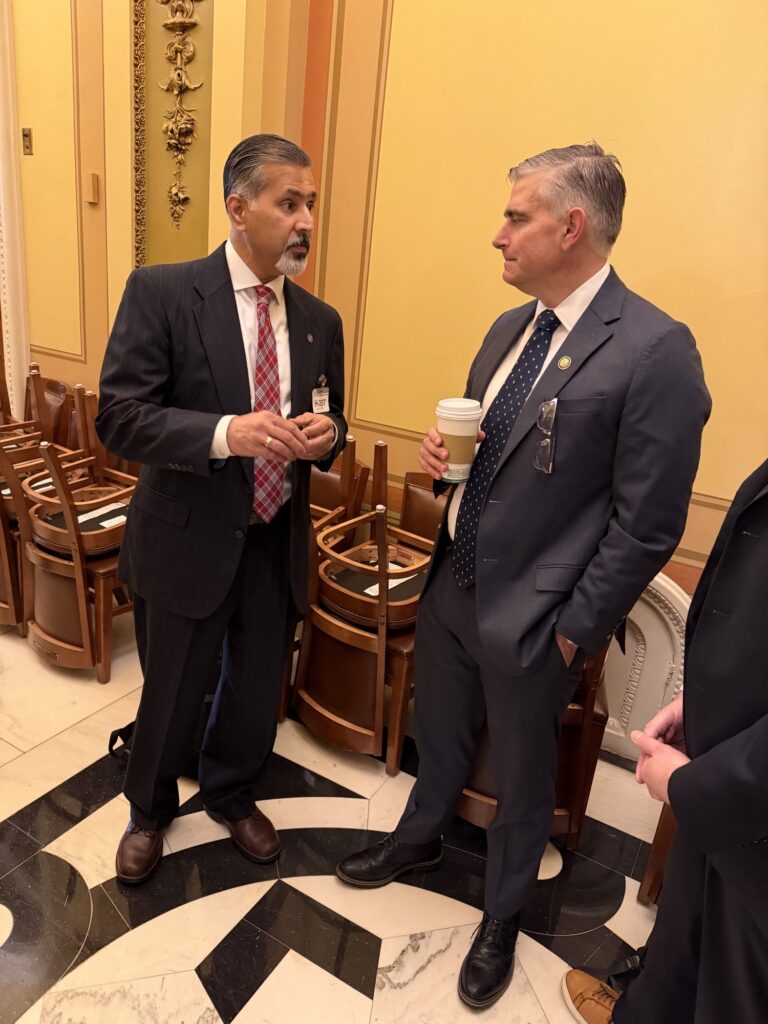 Two men in suits and ties stand together, conversing.
