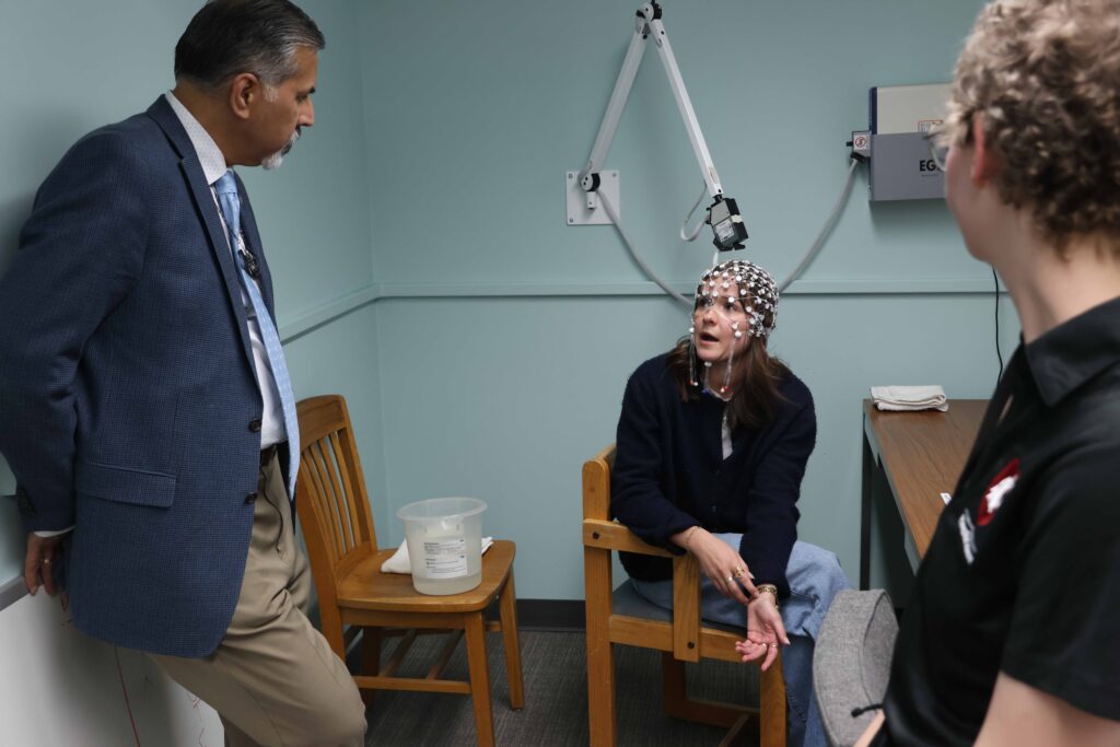 Raj Khosla looks at Taylor Schillinger, who is wearing an electrode device on her head that tracks signals emitted by the brain. Ashley Murray looks on.