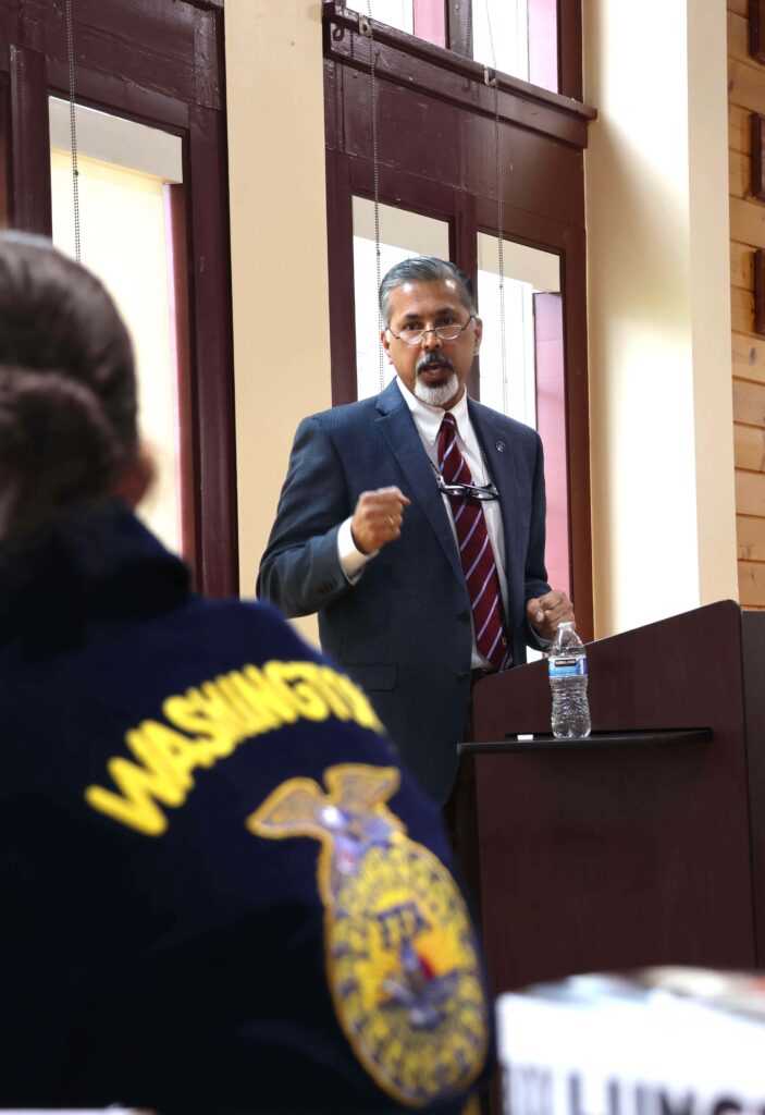 Raj Khosla stands at a podium while speaking. The back of an FFA student is in the foreground.