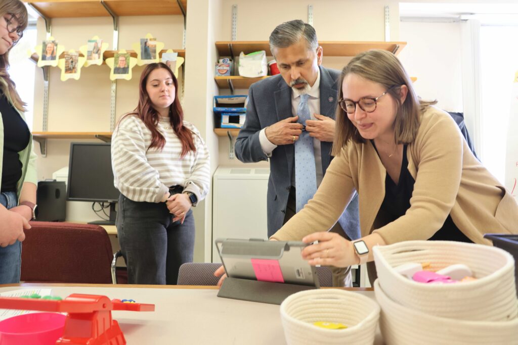 Raj Khosla leans over to look at a screen held by Nicole Scalise as she demonstrates an app. Two students look on.