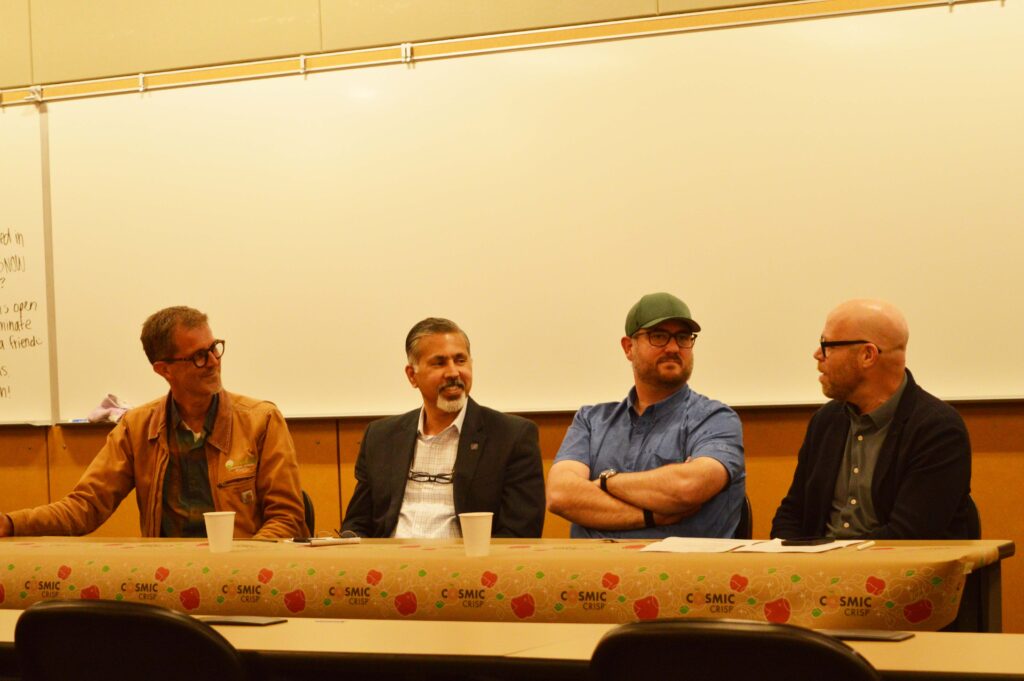 Four people seated in front of a whiteboard at a long table with a Cosmic Crisp tablecloth on it.