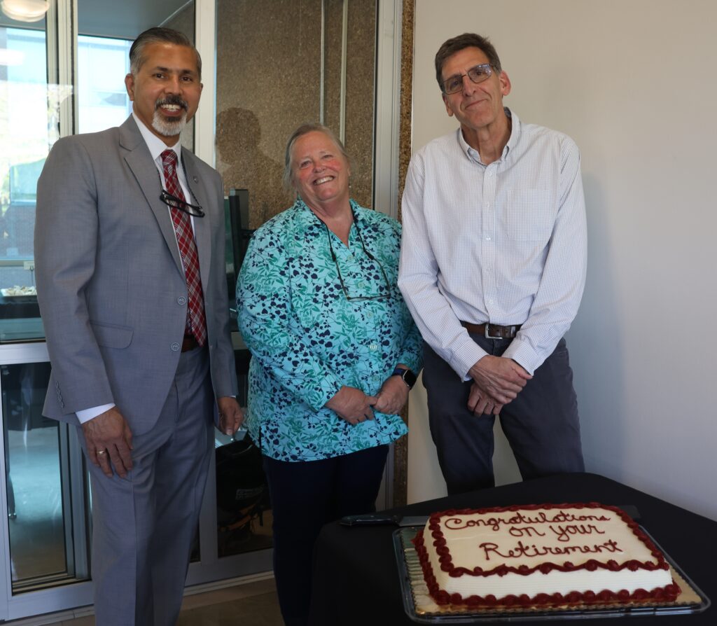 Raj Khosla, Karen Lewis, and Scot Hulbert stand next to a cake that reads "Congratulations on your retirement."