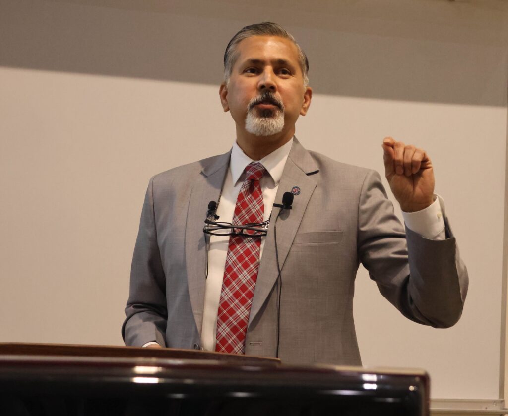 Raj Khosla gestures while speaking at a podium.