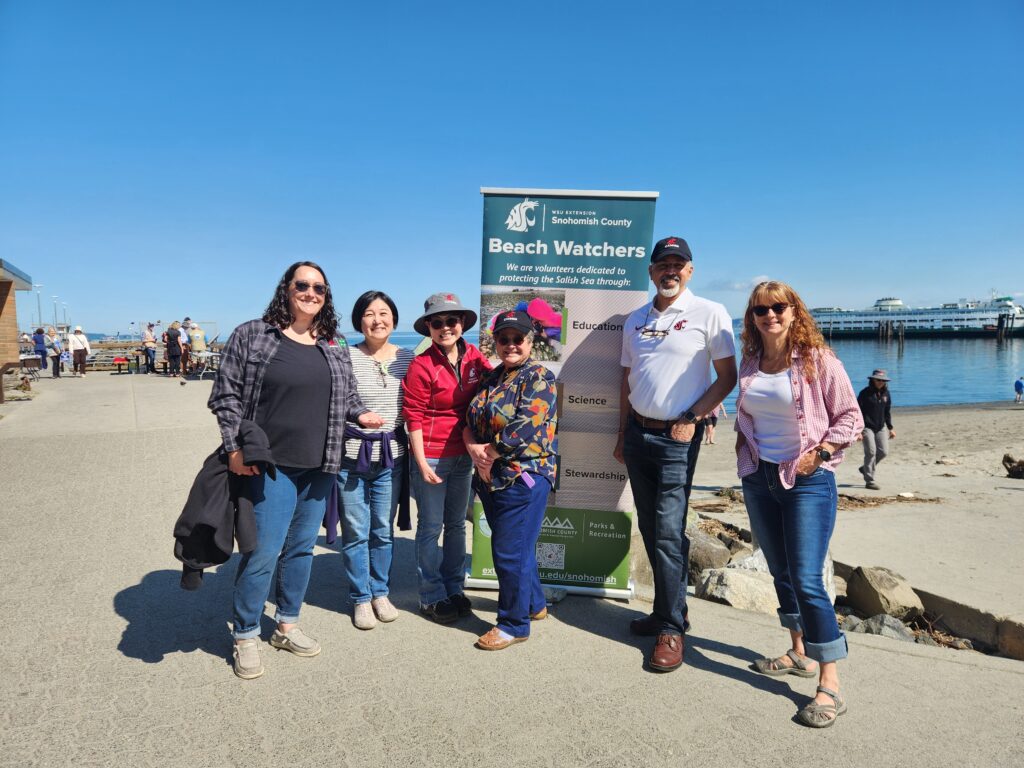 Six people stand next to a sign with information about the WSU Extension Beach Watchers Program.