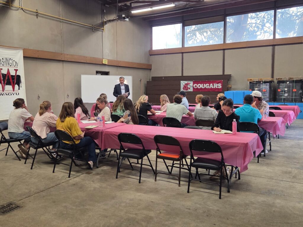 Raj Khosla speaks to students who are seated at tables with folding chairs inside the WSU Beef Center.