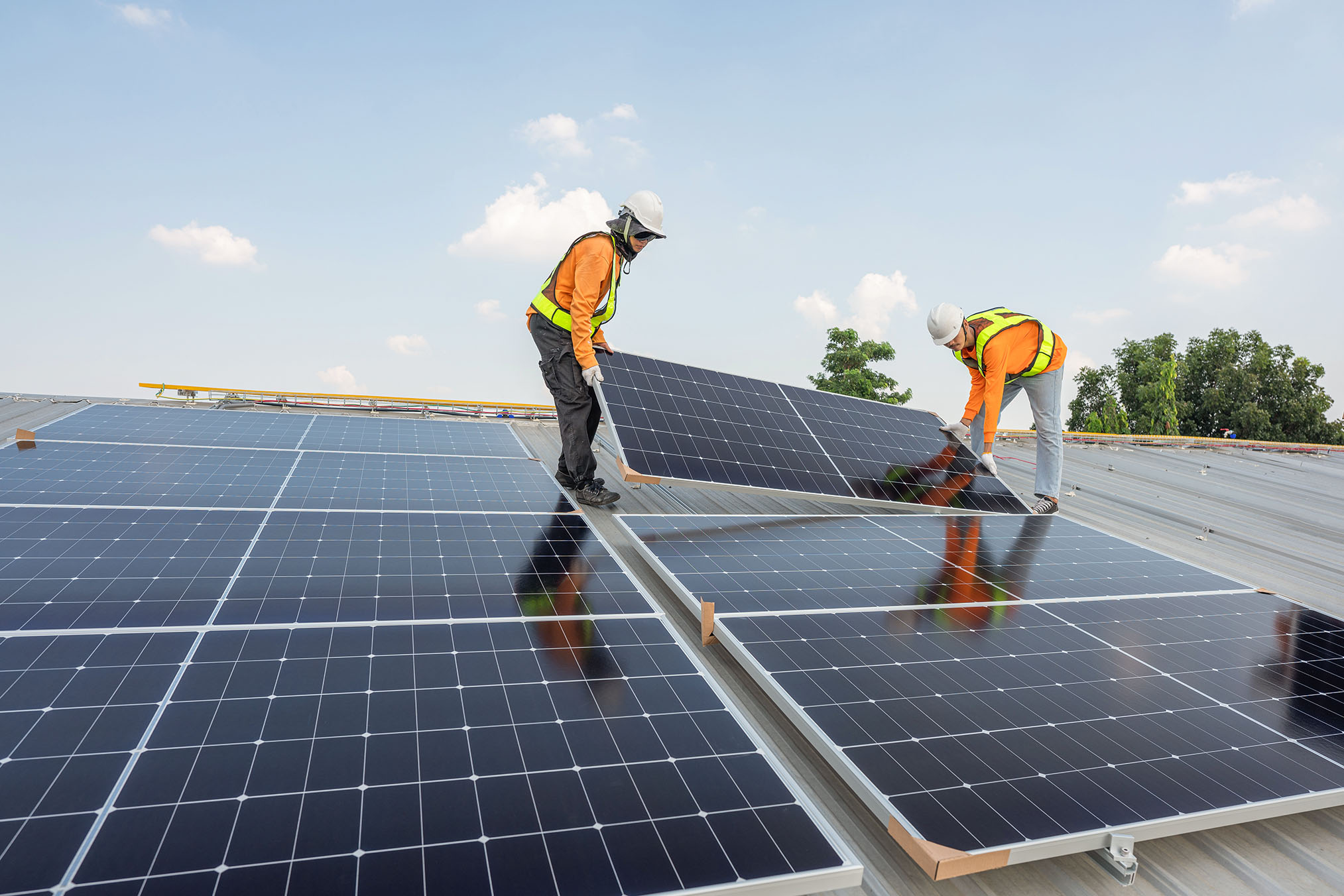 Two people installing solar panels on a roof.