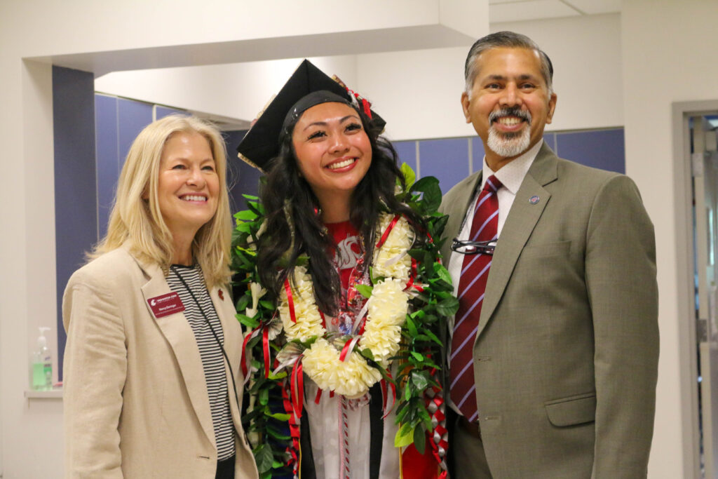 Raj and Nancy Deringer stand with a student dressed in a cap and gown.