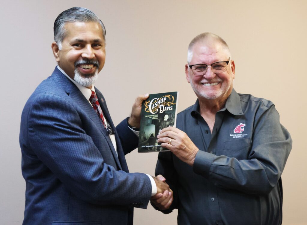 Raj and Gordon shake hands while holding a book about Cashup Davis.