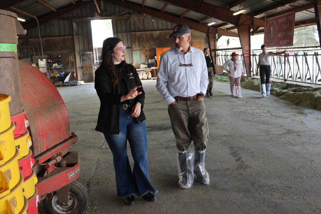 Raj Khosla and Addison Carroll walk through a dairy barn. Several other people are walking in the background.