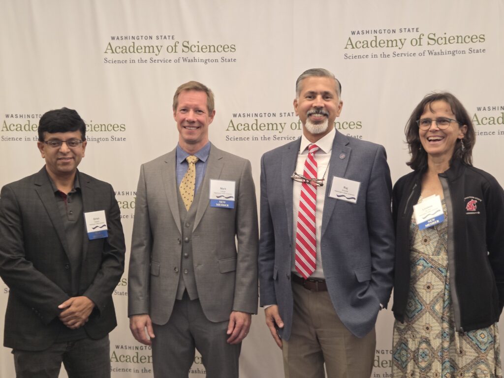 Four people stand in front of a background that has the words "Washington State Academy of Sciences Science in the Service of Washington state" repeated on it.