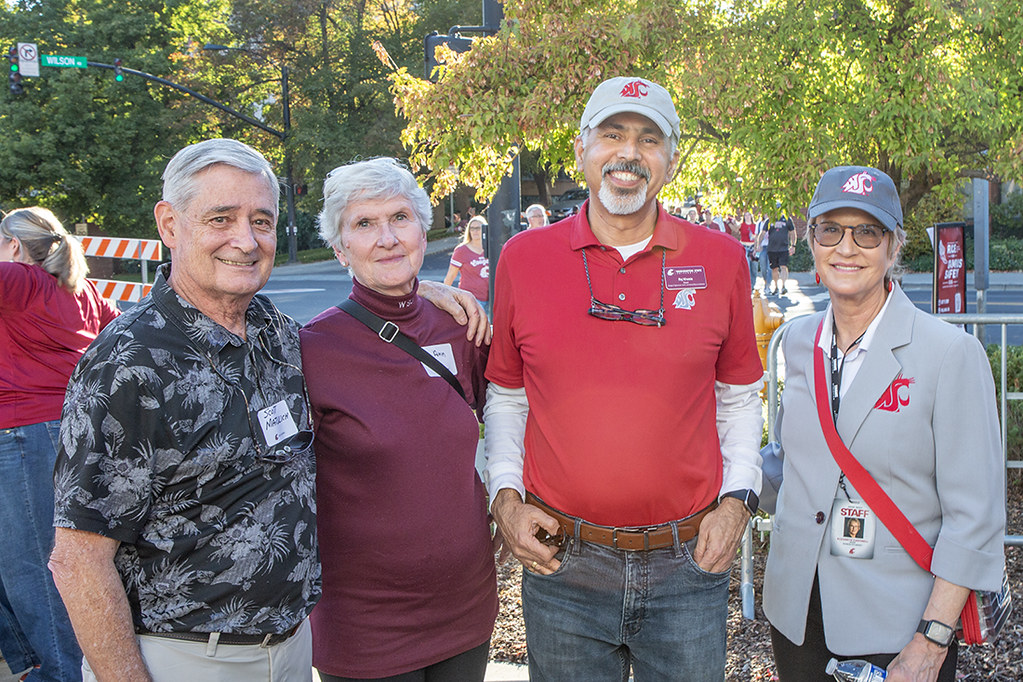 Four people stand together outside, smiling.