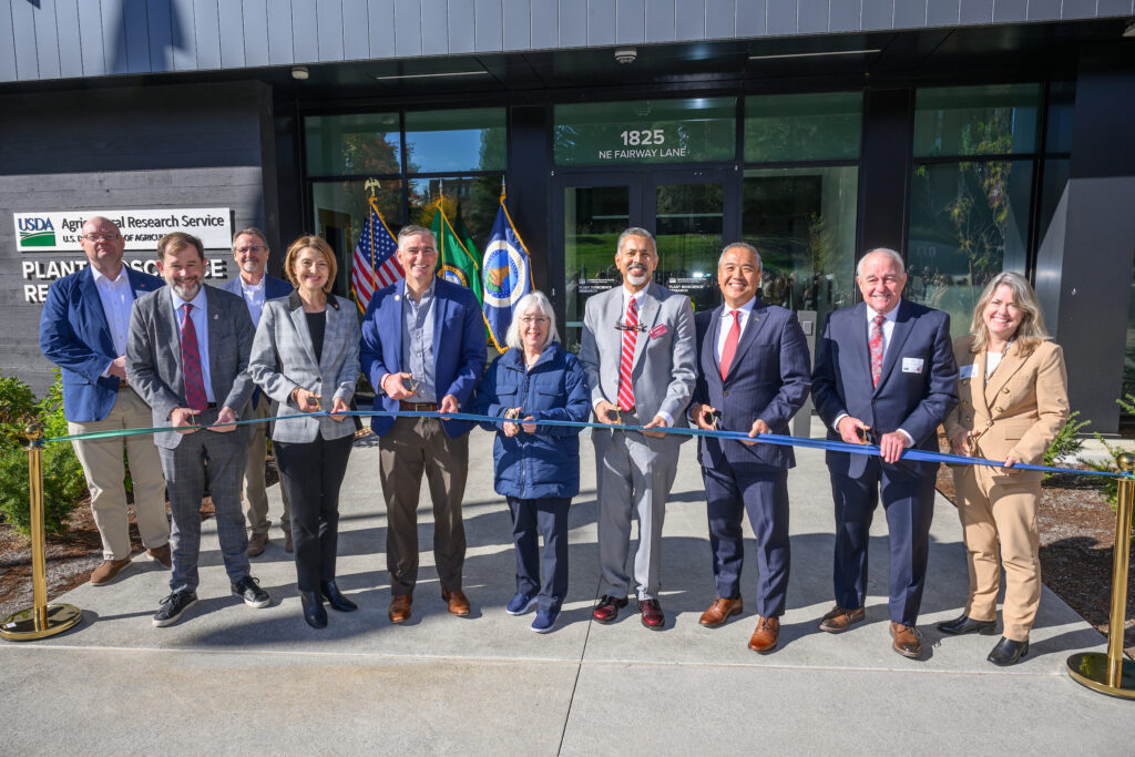 A group of ten people prepares to cut a ribbon in front of the USDA ARS building.