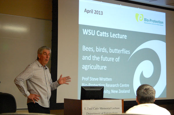 A man stands next to a projector screen that says, "WSU Catts Lecture. Bees, birds, butterflies, and the future of agriculture."