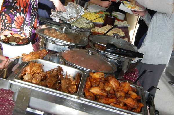 Lots of food is laid out on a table as people fill their plates.