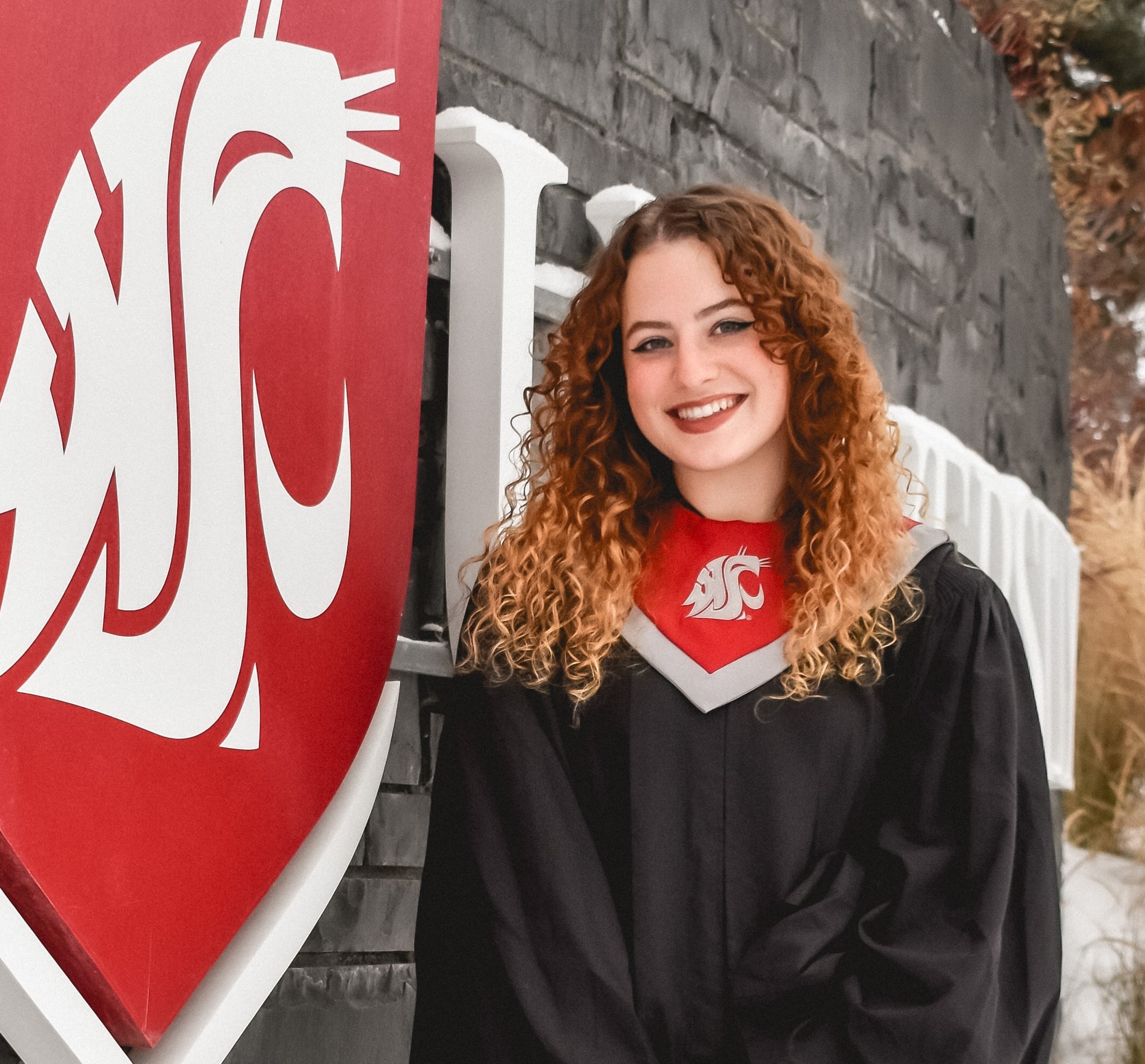 A student in graduate attire stands next to a WSU statue.