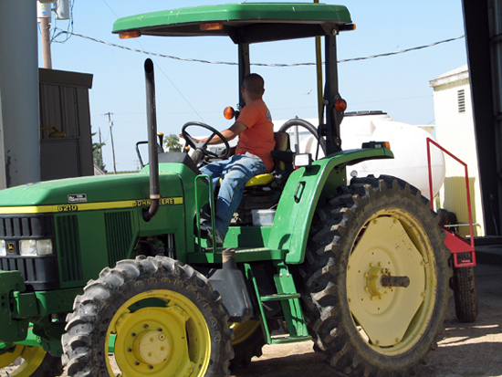 A picture of a man driving a John Deere 6210 tractor.