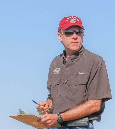 Photo of Mark J. Pavek holding a clipboard while working on the WSU research farm in Othello