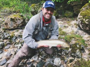 Photo of Zach Holden holding a fish near the stream where he caught it