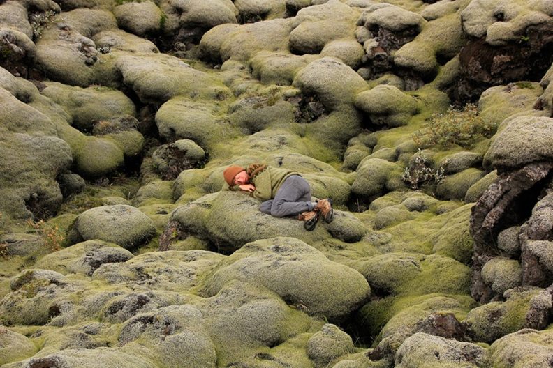 Photograph of person resting on mossy rocks. 
