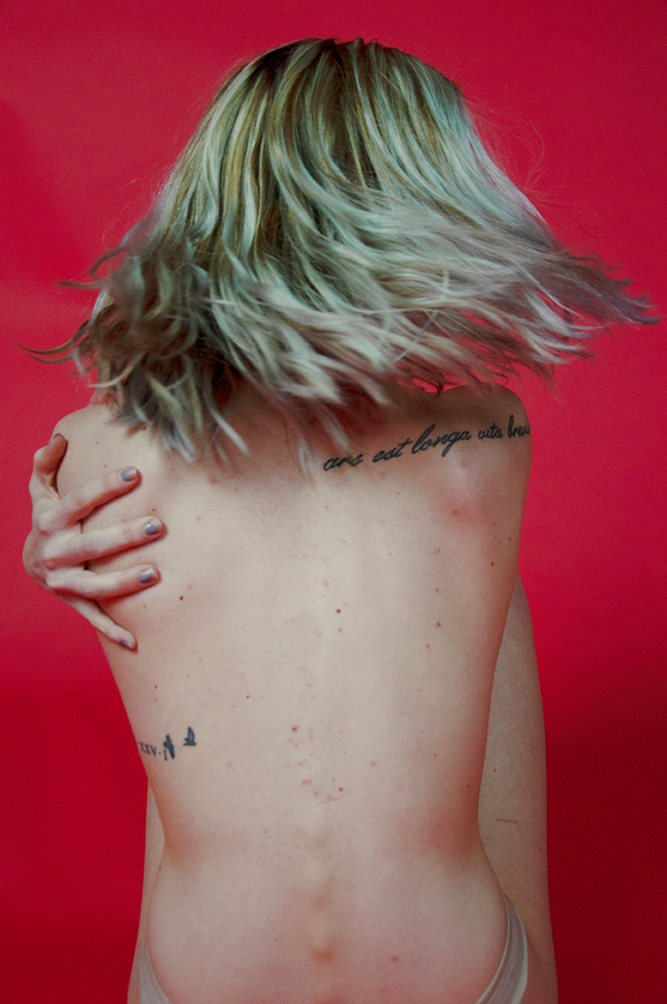 Photograph of person's bare back caught in motion with blond hair flying outward as she turns.