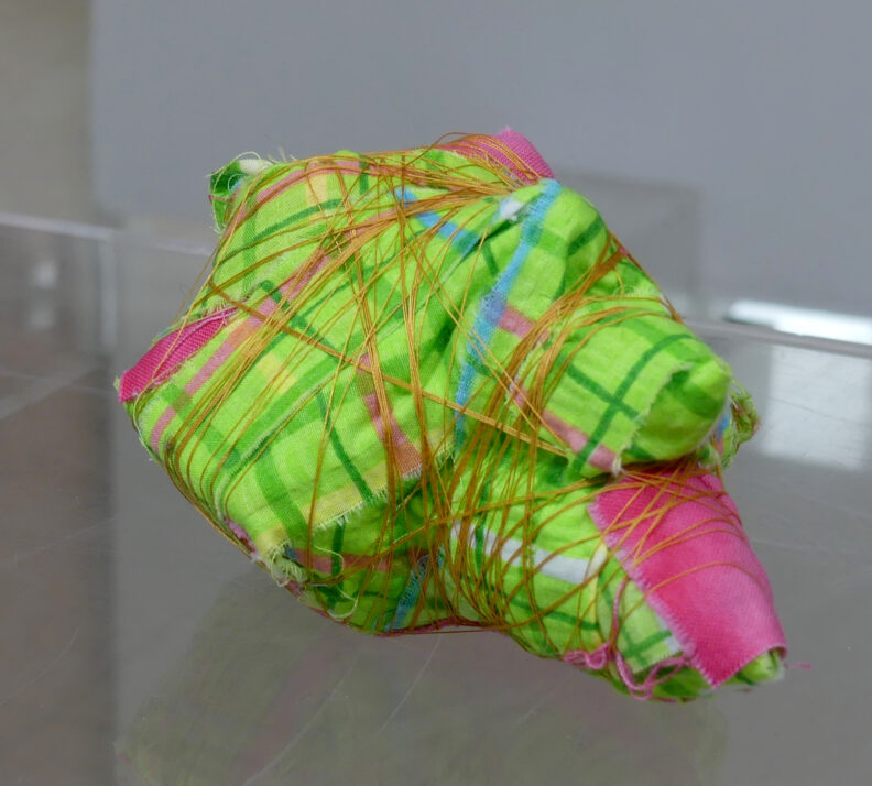 Fabric sculpture of green plaid fabric wrapped in gold thread.
