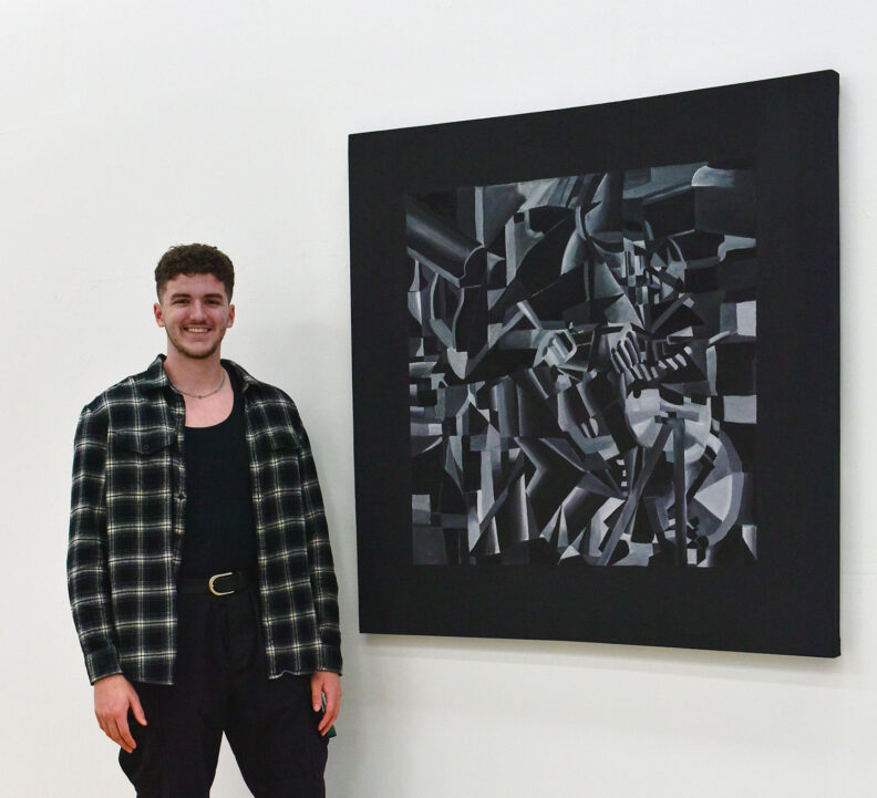 Student standing next to 2D artwork in gallery.