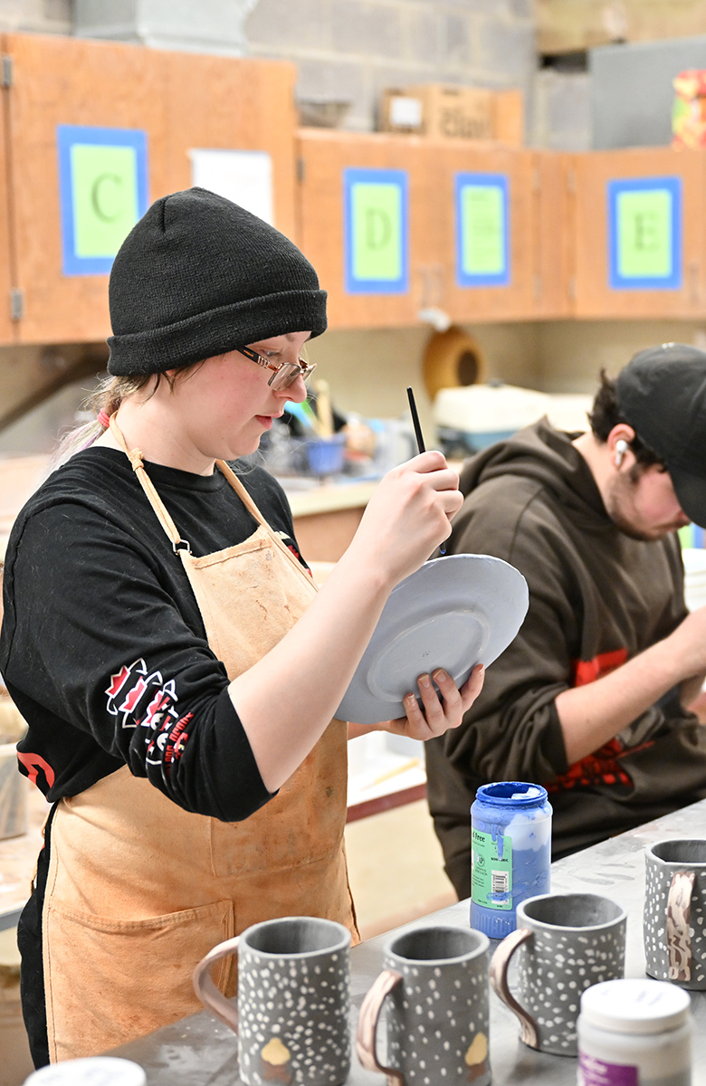 Two students painting ceramics in studio.