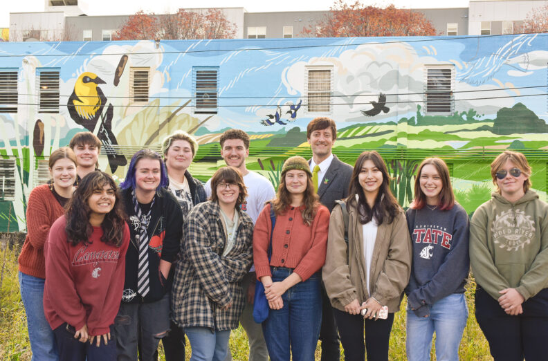 Photo of students and teacher in front of building with mural.