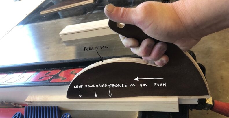 Demonstration of cutting material using the push stick. Keep downward pressure as you push. Image links to larger version.