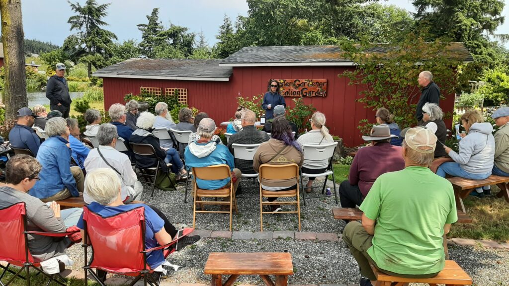 People seated outdoors listening to a gardening presentation.
